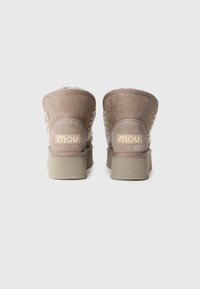 Botine din suede, de culoare maronie deschisă, cu un material superior texturat, căptușeală din blană sintetică și un logo subtil pe toc, având o talpă căptușită.