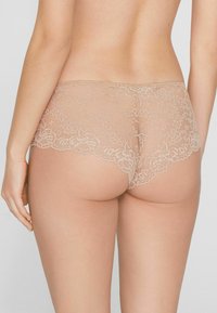 Braguitas hipster de encaje en color nude, con bordes con ondas y diseño floral. Tejido suave y ligero con textura transparente.