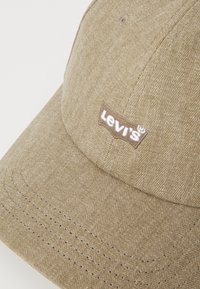 Brun herringbone cap med sømte detaljer og en brun Levi's logo lapp foran. Laget av teksturert stoff med buet skjerm.
