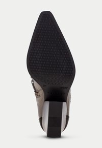 Zapato de tacón con un upper texturizado de color beige, una suela de goma negra resistente con un diseño de banda de rodadura, y un acento metálico cerca de la cremallera.