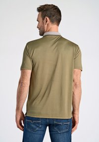 Olivgrön polo-skjorta med en grå krage, korta ärmar och en mjuk textur. Har sidofickor och en rak fåll. Bärs med blå jeans.