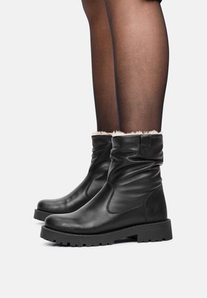 Botas de tobillo de cuero negro con un diseño holgado, que presentan un forro de piel sintética en la parte superior y una suela de goma resistente.