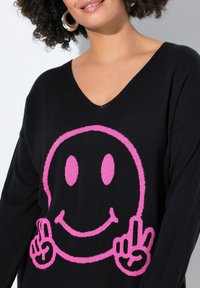 Maglione nero a maglia con una grande grafica di una faccia sorridente rosa con due medi alzati. Design a V e texture morbida.