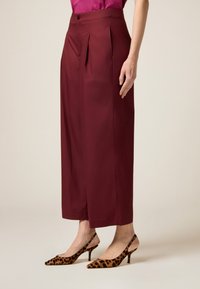 Bordeaux wijde broek met plooien aan de voorkant, hoge taille en knoopsluiting, gecombineerd met leopardprint hakken met puntige neuzen en spitse hakken.