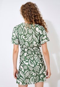 Grünes Blumenkleid mit einem weißen Paisleymuster, kurzen Ärmeln und einem elastischen Taillenbund zur Betonung der Silhouette. Glatter Stoff.