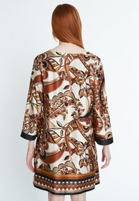 Kurzes Kleid aus Satin, mit einem beigen Grundton, braunen Blumen- und abstrakten Mustern sowie einem schwarzen Saumakzent.