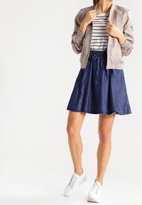 Lichte beige bomberjack over een gestreept wit en zwart T-shirt. Een marineblauwe A-lijn rok en witte sneakers maken de outfit compleet.