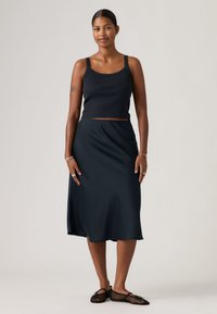 Haut court bleu marine et jupe midi assortie à la texture lisse. La tenue est complétée par des ballerines noires en mesh.