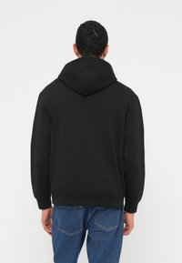 Sweatshirt preta com capuz, textura suave e corte descontraído. Apresenta bainha e punhos canelados, combinados com jeans de ganga azul.