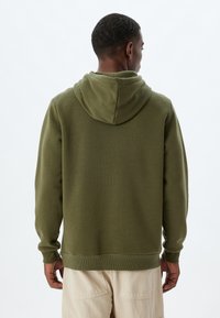 Sudadera de color verde oliva con capucha ajustable, puños y dobladillo acanalados. Textura suave, diseño simple y sin logotipos ni patrones visibles.