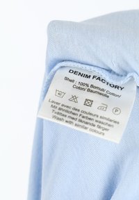 Light blue cotton fabric with care label, displaying washing instructions and brand name "DENIM FACTORY." Smooth texture, soft appearance.