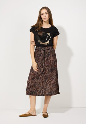 T-shirt noir avec un graphique en sequins ; jupe maxi à motifs marron ; chaussures plates marron à enfiler. Coupe décontractée, tissu doux et taille ajustable.