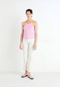 Lichtroze geribbelde tanktop met oranje trim, gecombineerd met witte flare broeken en sandaaltjes met bandjes. Eenvoudig ontwerp, casual stijl.