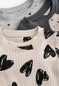 Tre magliette a maniche corte: grigia con cuori neri, grigio scuro a coste e beige con motivi a cuori neri; tutte presentano colli a giro e tessuto leggero.