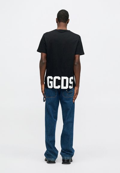 Čierne bavlnené tričko s krátkym rukávom a veľkým bielym logom "GCDS" na leme. V kombinácii s modrými džínsami, ktoré majú uvoľnený strih.