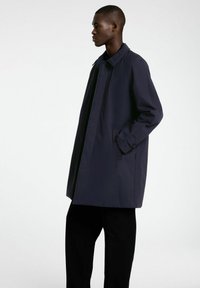 Mornarsko modra bunda s ovratnikom, stranskimi žepi in ravnim krojem. Ima dolge rokave in gladko teksturo tkanine.