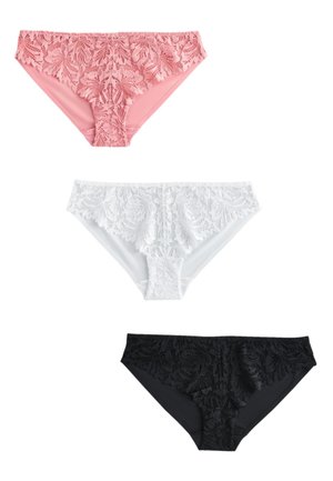 Kobieta z długimi ciemnymi włosami, ubrana w biały rozpinany sweter, biały koronkowy biustonosz i dopasowaną koronkową bieliznę, stoi na jednolitym tle.