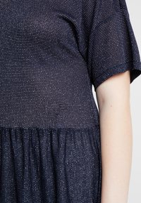 Marinblå klänning med korta ärmar, i en strukturerad tyg med vita horisontella ränder och en rynkad midja. Mjuk, lätt material.