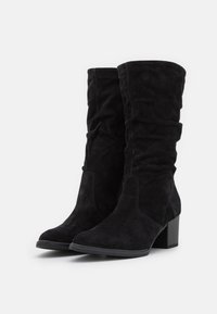 Bottes noires en daim jusqu'au genou avec un design froncé, des talons carrés et une texture lisse. Elles comportent des coutures renforcées et des bouts arrondis.
