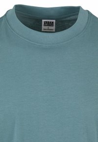 Světle modré bavlněné tričko s kulatým výstřihem a krátkými rukávy. Textura je hladká, obsahuje štítek s nápisem "Urban Classics."