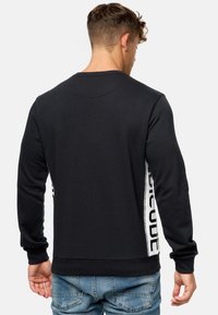 Sort sweatshirt med lange ærmer, der har sidelister med tekst, rund hals og en glat, blød tekstur. Bagview synlig.