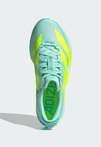 Scarpa sportiva in aqua e giallo neon con parte superiore in rete, superficie testurizzata, lacci piatti e marchio ben visibile sulla soletta e sul lato laterale.