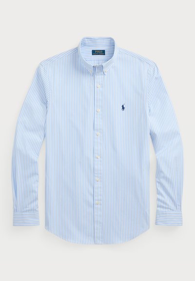 Vaaleansininen raidallinen nappikauluspaita, pitkät hihat, valkoiset napit, klassinen kaulus, jossa on pieni tummansininen logo vasemmalla rinnassa. Puuvillakangasta.