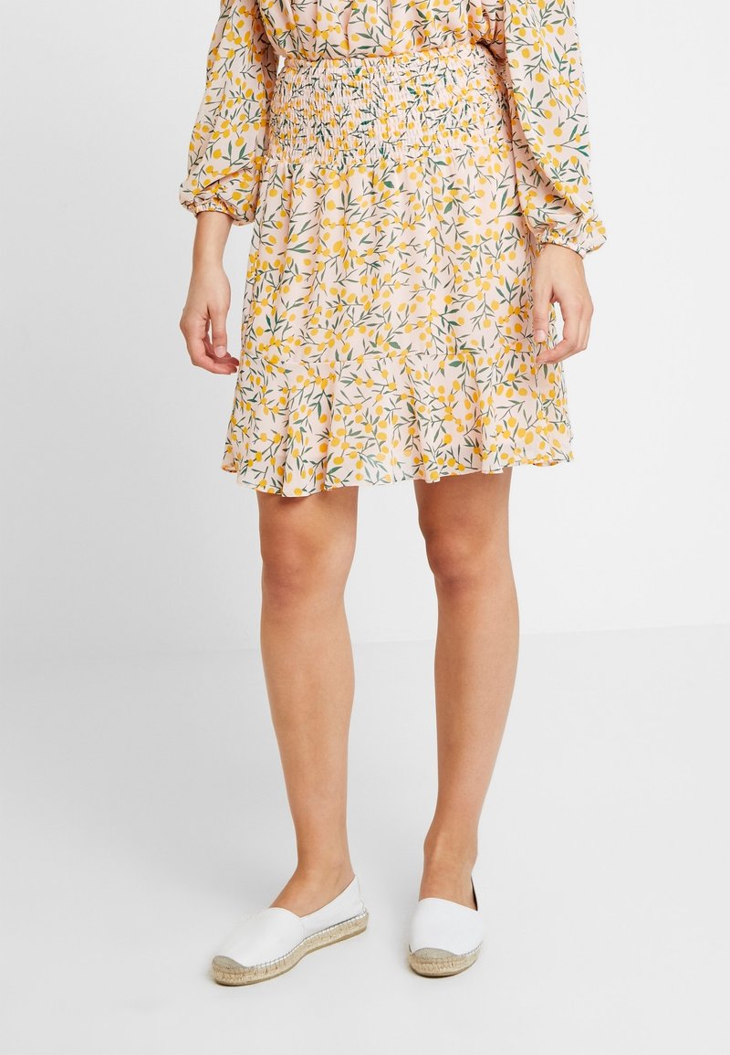 Jupe à motif floral avec détails jaunes et verts, tissu léger, taille smockée, ourlet à volants, portée avec des espadrilles blanches.