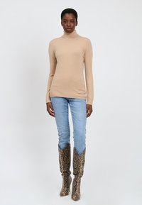 Maglione beige a collo alto, slim-fit, abbinato a jeans azzurri chiari e stivali fino al ginocchio con stampa serpente, punta affusolata e top a forma di V.