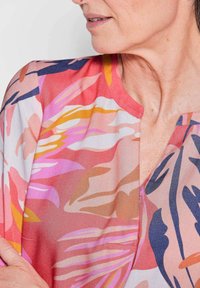 Blumenbluse in rosa, orange und blauen Mustern. Leichter, glatter Stoff mit V-Ausschnitt und kurzen Ärmeln. Keine Knöpfe oder Beschläge.