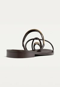 Ruske, flate sandaler med tynne, buede stropper og en metallisk detalj. Glatt tekstur med rund tå og svak hæl for støtte.