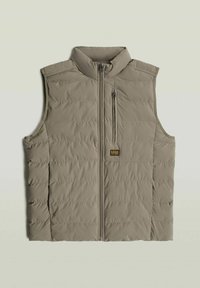 Gilet smanicato beige trapuntato con collo alto, zip frontale e taschino sul lato sinistro con etichetta del marchio. Texture liscia, design minimalista.