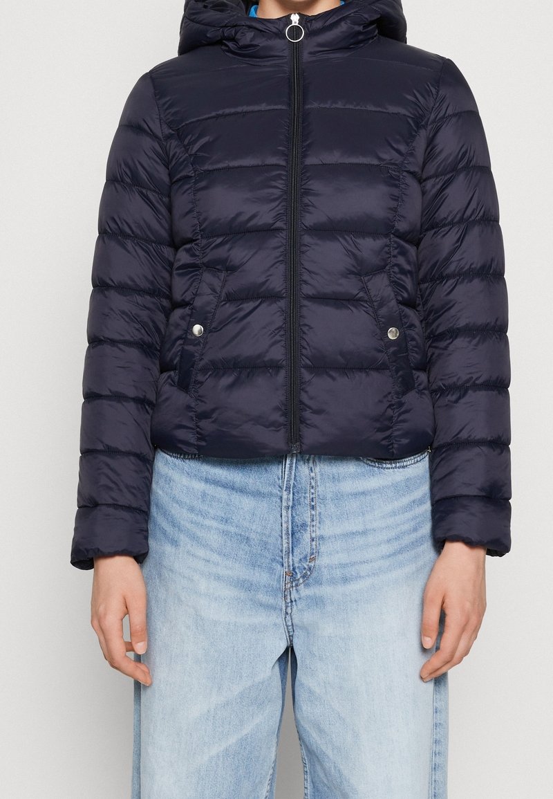 Mörkblå puffjacka med huva, dragkedja framtill och tryckknappar; har sydda paneler och en glänsande finish.