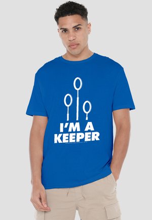 Man wearing blue T-shirt with three white Quidditch goal hoops and text "I'M A KEEPER" in bold white letters.