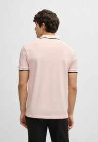 Polo shirt rosa chiaro con maniche corte, rifiniture nere sul colletto e sulle maniche, realizzato in tessuto liscio. La vista posteriore mostra dettagli minimi.