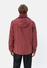 Giacca impermeabile bordeaux con cappuccio, polsini elasticizzati, dettagli riflettenti e logo sul retro. Tessuto liscio, design ergonomico.