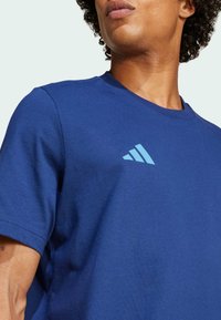 Blauwe katoenen t-shirt met korte mouwen, voorzien van een lichtblauw Adidas-logo op de bovenste linkerborst. Gladde textuur, klassiek ronde halsontwerp.
