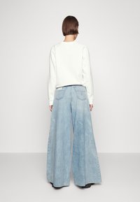 Felpa grigia chiara abbinata a jeans in denim blu sbiaditi a gamba larga, con tasche posteriori e un design pulito e minimalista.