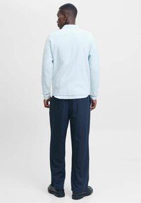 Lyseblå, struktureret sweater med ribbede manchetter og kant, sammen med mørke stribede bukser og sorte sko. Set fra ryggen.