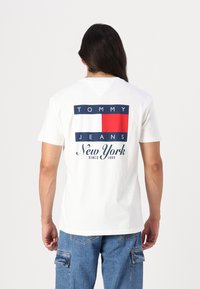 Hvit kortermet t-skjorte med grafisk design i marineblått og rødt, med "TOMMY JEANS" og "New York, siden 1985" på ryggen.