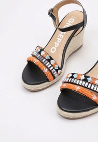 Sandali con zeppa neri con cinturini in perline arancioni, bianchi e blu, dotati di una suola in espadrille strutturata e di un cinturino alla caviglia per supporto.