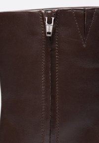 Brown leather boot featuring a YKK zipper, prominent stitching, and a smooth texture with a structured design.