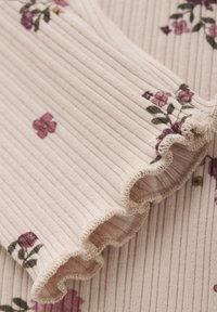 Top en tissu côtelé rose clair avec broderies florales. Il présente des bords froncés et des détails texturés, mettant en valeur des accents violets et verts.