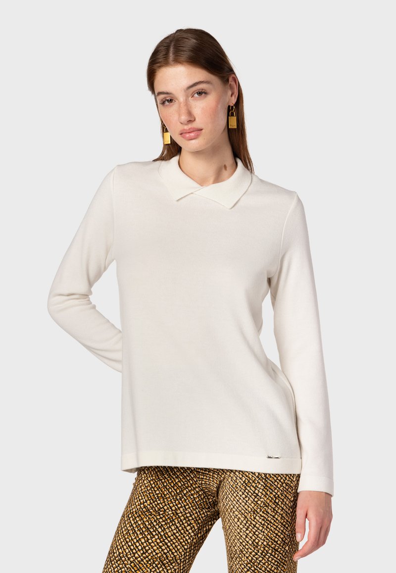Maglione bianco a maniche lunghe con colletto, realizzato in tessuto morbido; presenta una texture sottile. Abbinato a pantaloni marroni con stampa.