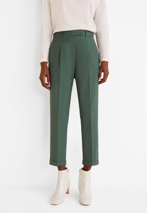 Pantalones verdes ajustados de tela suave, con pliegues y pierna recortada. Combinados conbotines blancos de tobillo con tacón cuadrado.