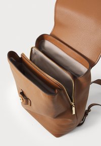 Sac à dos en cuir marron avec un extérieur texturé, deux compartiments zippés et une doublure intérieure lisse. Doté d'accents en métal doré.