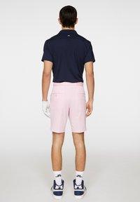 Navy-paitainen polo-paita lyhyillä hihoilla; vaaleanpunaiset suoralahkeiset shortsit; valkoinen hansikas; siniset ja valkoiset kengät; näkyvät takanapit ja taskut shortseissa.