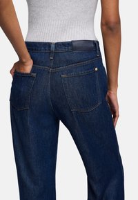 Dunkelblaue Jeans aus Denim mit einer hohen Taille, ausgestattet mit Gesäßtaschen, einem Lederpatch am Bund und feinen Nähten.