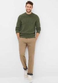 Grüner gestrickter Pullover mit Rundhalsausschnitt, kombiniert mit beigen Hosen und hellen Sneakers. Das Outfit hat einen lässigen, lockeren Schnitt.