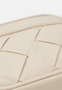 Borsa beige trapuntata in ecopelle con una superficie liscia, caratterizzata da un motivo a quadrati e un bordo cucito per una maggiore struttura.